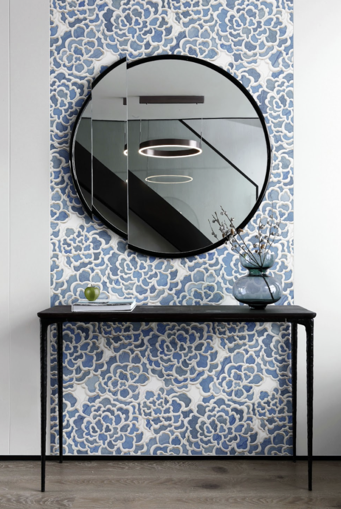 Azul Fiore waterjet mosaic in Calacatta Oro with brushed brass and mixed green porcelain accents, installed as a decorative blue floral feature wall behind a round mirror.